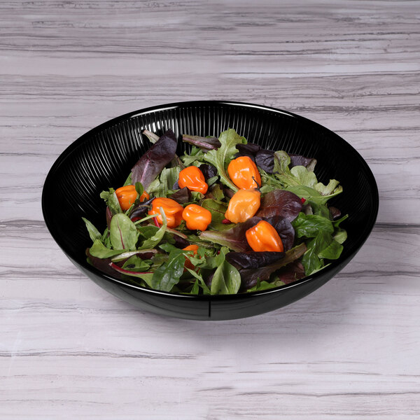 A black Elite Global Solutions Sunburst melamine bowl filled with salad and orange peppers on a wood surface.
