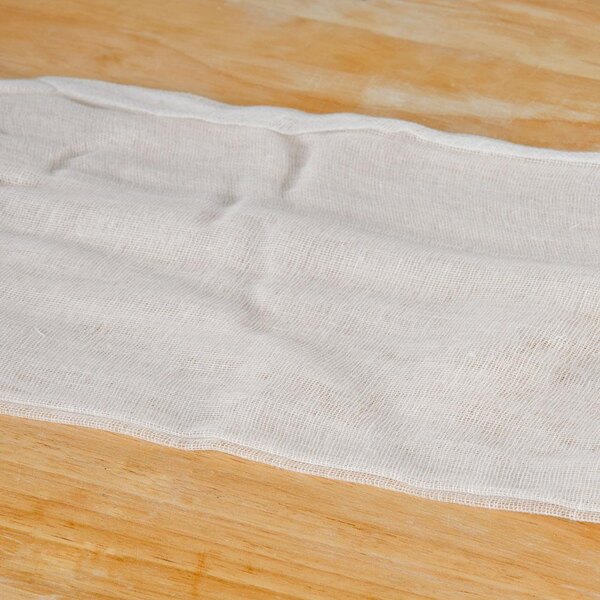 A roll of San Jamar Grade 40 bleached cheesecloth on a wooden surface.