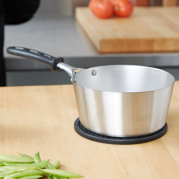 A Vollrath stainless steel sauce pan with a black silicone handle on a stove.