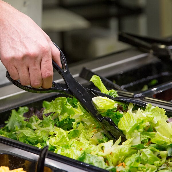 A person using Fineline black plastic salad tongs to serve a salad.
