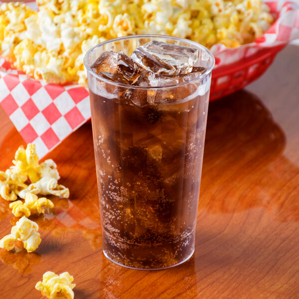 A Fineline clear plastic tumbler filled with soda and ice on a table with a basket of popcorn.