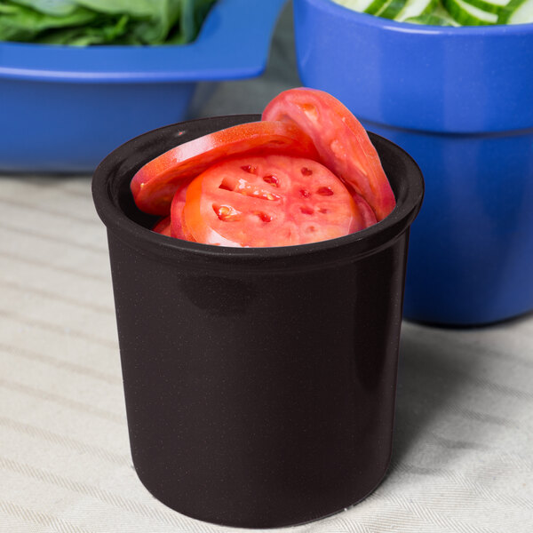 A black Tablecraft cast aluminum condiment bowl with sliced tomatoes in it on a counter.