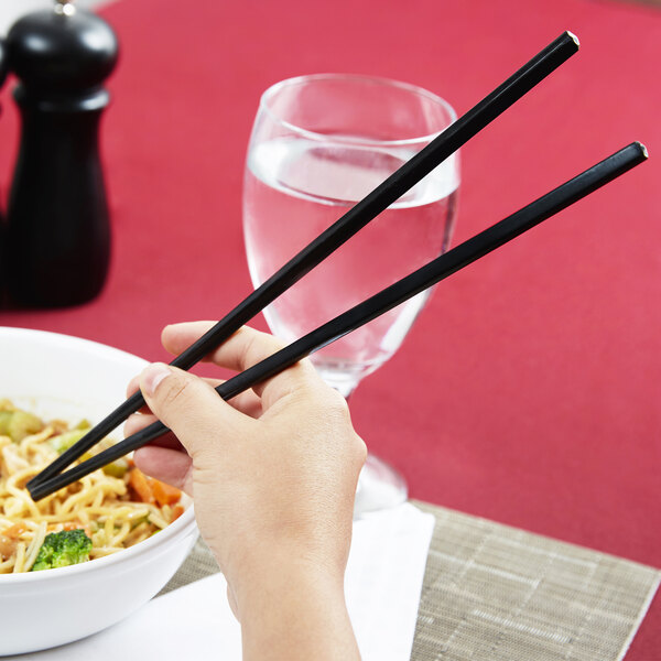 A hand using Town black plastic chopsticks to eat noodles.