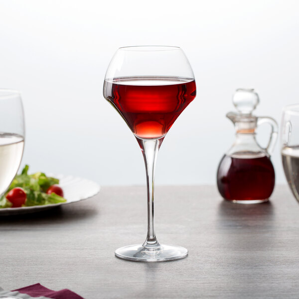 A close-up of a Chef & Sommelier wine glass filled with red wine on a table.