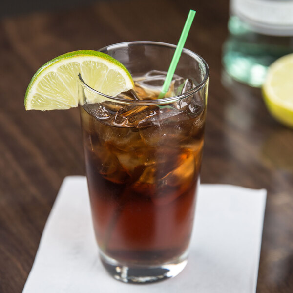 A highball glass of iced tea with a straw and a lime wedge.