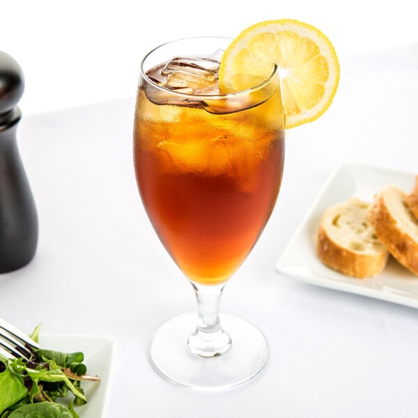 An Arcoroc iced tea glass filled with iced tea and a lemon slice on top.