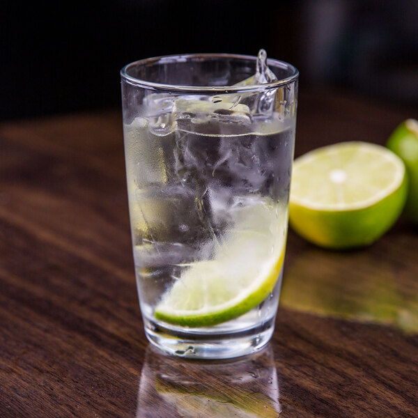 A Arcoroc Excalibur highball glass with ice water and a lime slice.