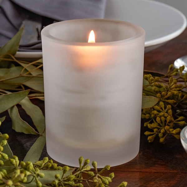 A Sterno petite frosted glass votive candle holder with a lit candle on a table.