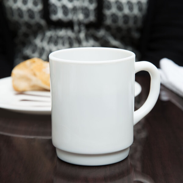 An Arcoroc white stacking mug on a table.