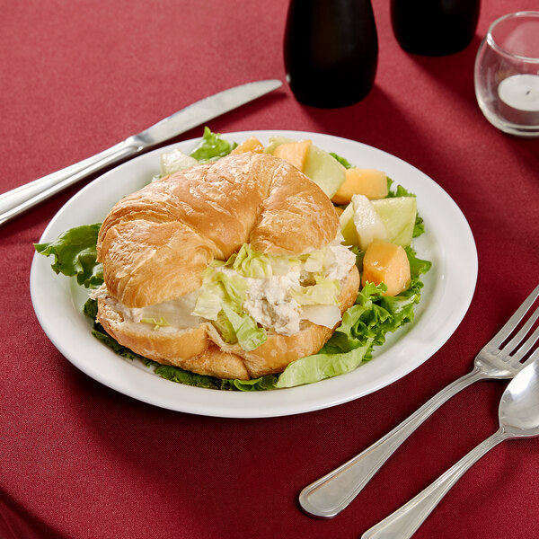 A plate with a croissant sandwich, salad, and fruit on it.