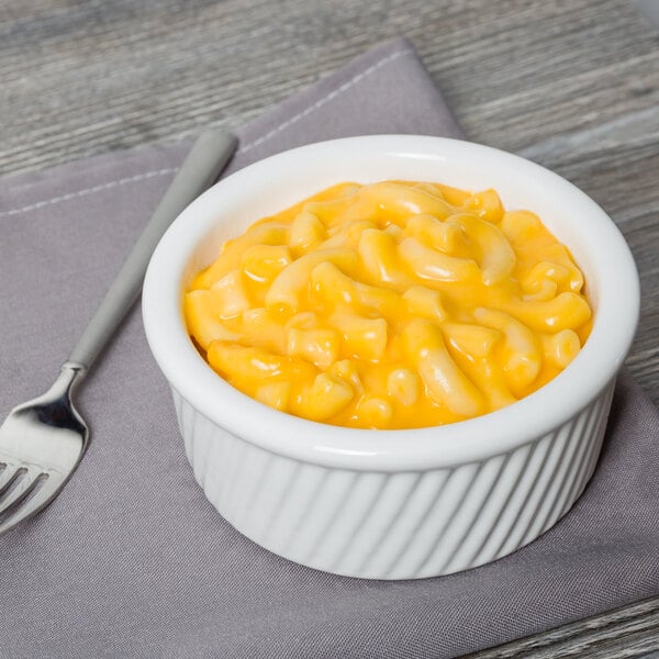A Tuxton white china ramekin filled with macaroni and cheese with a spoon.