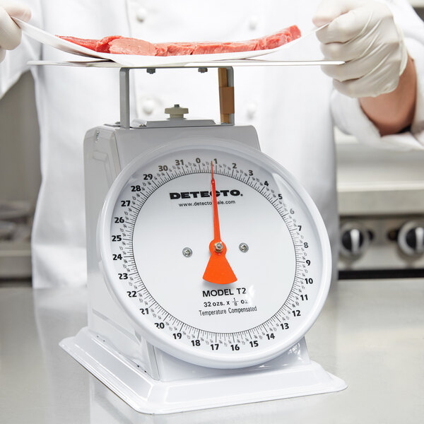 A person weighing meat on a Cardinal Detecto mechanical portion scale.