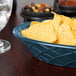 A blue oval polyethylene basket filled with chips on a table next to a glass of water.
