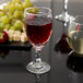 A close-up of a Libbey wine glass filled with red wine on a table next to grapes.