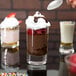 A spoon pouring chocolate pudding into an Arcoroc shot glass.