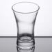 An Arcoroc clear glass shot glass with a curved rim on a table.