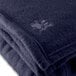 A close up of a navy blue Oxford fleece hotel blanket with a small embroidered logo.