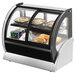A Vollrath curved glass countertop display case with food inside.