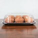 A Sabert black plastic catering tray with a high dome lid holding muffins on a table.