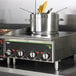 A Vollrath countertop induction hot plate with pots on it.