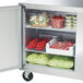 A Traulsen undercounter refrigerator with food inside, including a container of tomatoes.