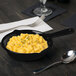 A Tablecraft black cast aluminum fry pan filled with macaroni and cheese on a table.