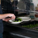 A person uses a black Cambro Sneeze Guard panel to serve themselves salad at a salad bar.
