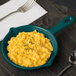 A Tablecraft hunter green cast aluminum fry pan filled with macaroni and cheese on a table.
