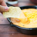 A person holding a Tablecraft black cast aluminum fry pan serving a chip dipped in cheese.