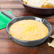 A Tablecraft gray cast aluminum fry pan filled with cheese dip next to a bowl of chips.