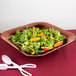 A salad in a copper square bowl with lettuce and carrots.