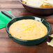 A Tablecraft hunter green cast aluminum fry pan filled with cheese dip next to a bowl of tortilla chips.