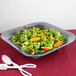 A gray Tablecraft square bowl of salad with carrots, lettuce, peppers, and tomatoes with spoons and forks.