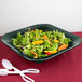 A salad with carrots, lettuce, peppers, and tomatoes in a hunter green square bowl.