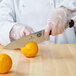 A person in a white coat using a Victorinox chef knife to cut an orange.