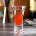 A Thunder Group plastic flared dessert shot glass filled with red liquid on a table in a cocktail bar.