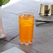 A Thunder Group heavy base highball glass filled with orange juice and ice on a table.