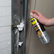 A hand holding a WD-40 spray can and spraying white foam on a door.