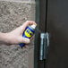 A hand holding a WD-40 spray can and spraying a door hinge.