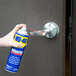 A person using WD-40 spray lubricant on a door handle.