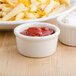 A white Tuxton china ramekin filled with ketchup on a table with a plate of cheese fries and french fries.