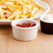 A Tuxton eggshell ramekin filled with ketchup next to a plate of french fries.