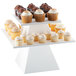 A white square pedestal cake stand with cupcakes on it.