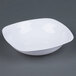 A white Fineline disposable plastic bowl on a gray surface.