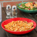 A red Sensation melamine bowl filled with pasta and salad on a table.