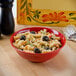 A red melamine bowl of pasta with black olives next to a fork.