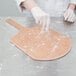 An American Metalcraft natural pizza peel with a person in gloves putting flour on a cutting board.