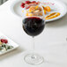 An Arcoroc Rutherford tall wine glass filled with red wine on a table with food.