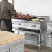 A man cooking food on a Cooking Performance Group gas countertop lava briquette charbroiler.