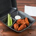 A black Dart foam container with three compartments holding chicken wings and celery sticks.